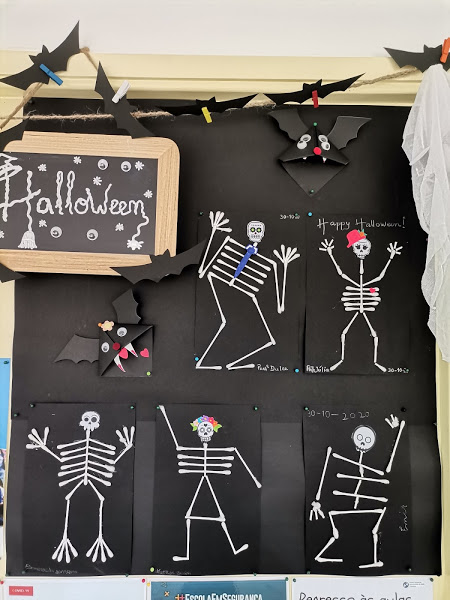 Esqueletos de cotonetes sobre cartolina preta, morcegos e lousa com texto "Hallowwen"