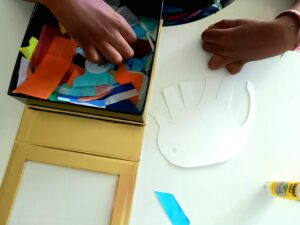 Um aluno escolhe papeis coloridos de uma caixa para enfeitar a forma de um elefante.