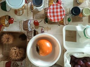 Frascos e frutos em cima da mesa: dióspiro, castanhas com os seus ouriços, uvas...