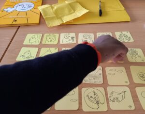 Um aluno joga o jogo dos abraços: a partir de cartas com desenhos de elementos que são mencionados no livro, o aluno deve formar pares que se abraçam.