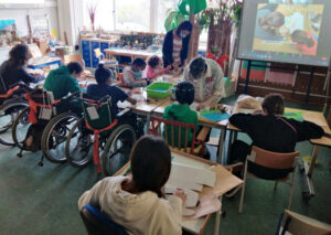 Visão global da sala de aula com os alunos a trabalhar ajudados pela professora e uma mãe que também assistiu à sessão.