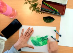 Um aluno a pintar com lápis de cera os verdes das suas folhas.