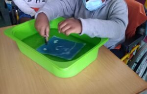 A mão de um aluno a lavar o seu trabalho dentro de uma tina com água.