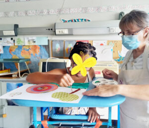 A professora ajuda uma aluna a segurar a sua composição artística.