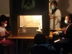 A apresentação de uma das peças de teatro: uma caixa de madeira iluminada com cenários e personagens de papel.
