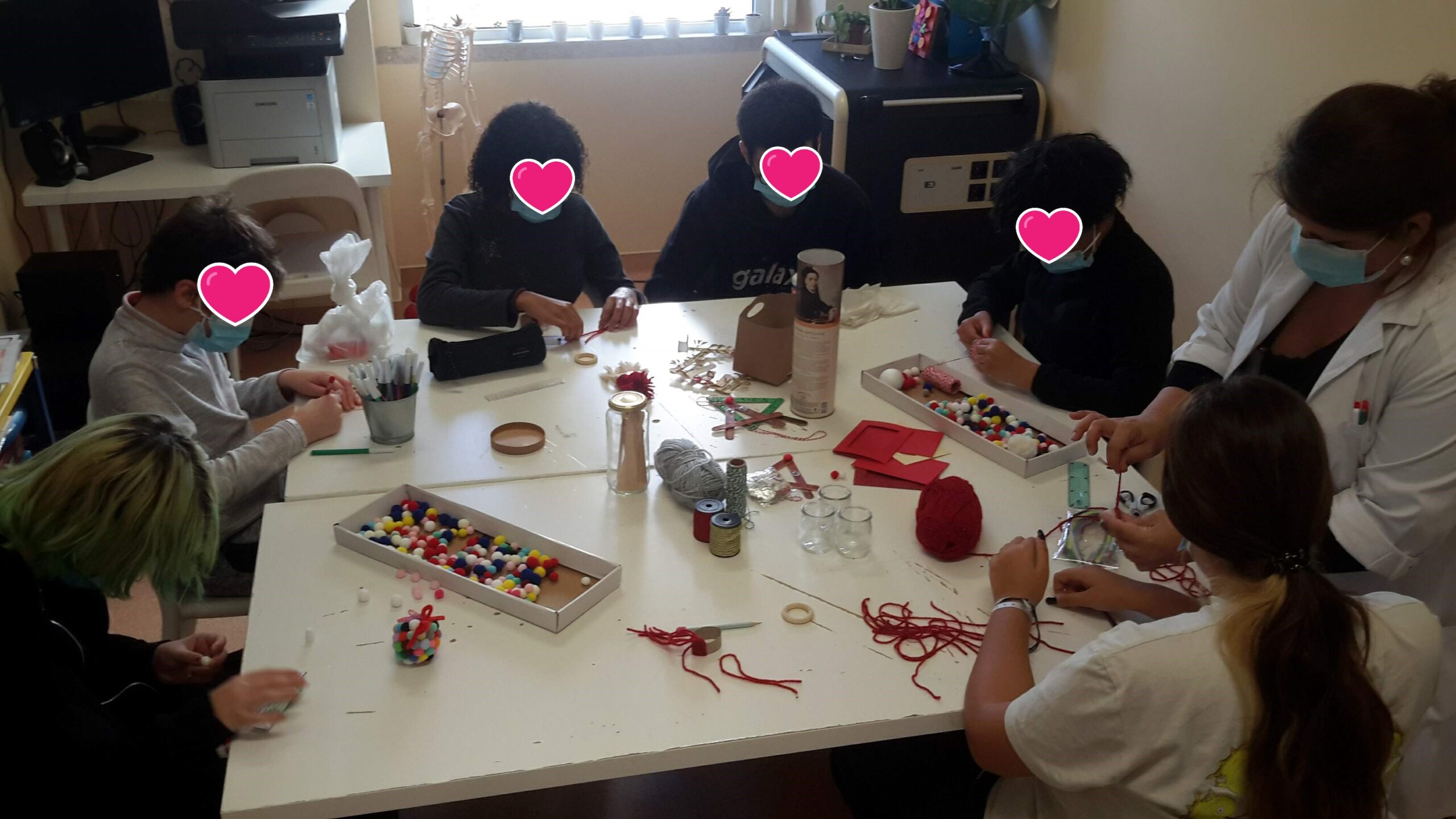 Alunos e professora a trabalhar sobre uma mesa com fio de lã, bolas de várias cores e outros materiais 