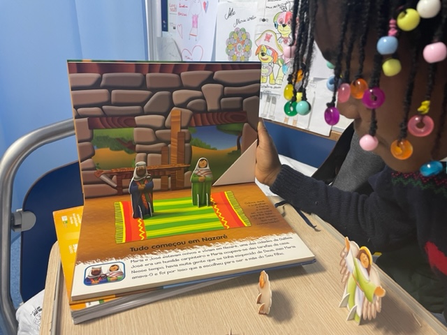 Criança abre um livro popup com duas figuras sobre um tapete numa casa de pedra