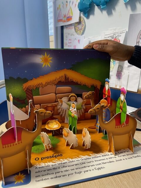Criança abre um livro popup com figuras do presépio com cabana em fundo