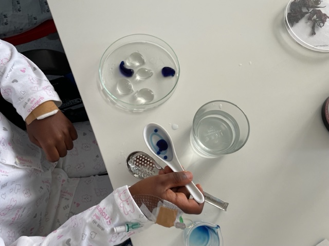 Criança com colher transporta bolhas azuis para um recipiente com água
