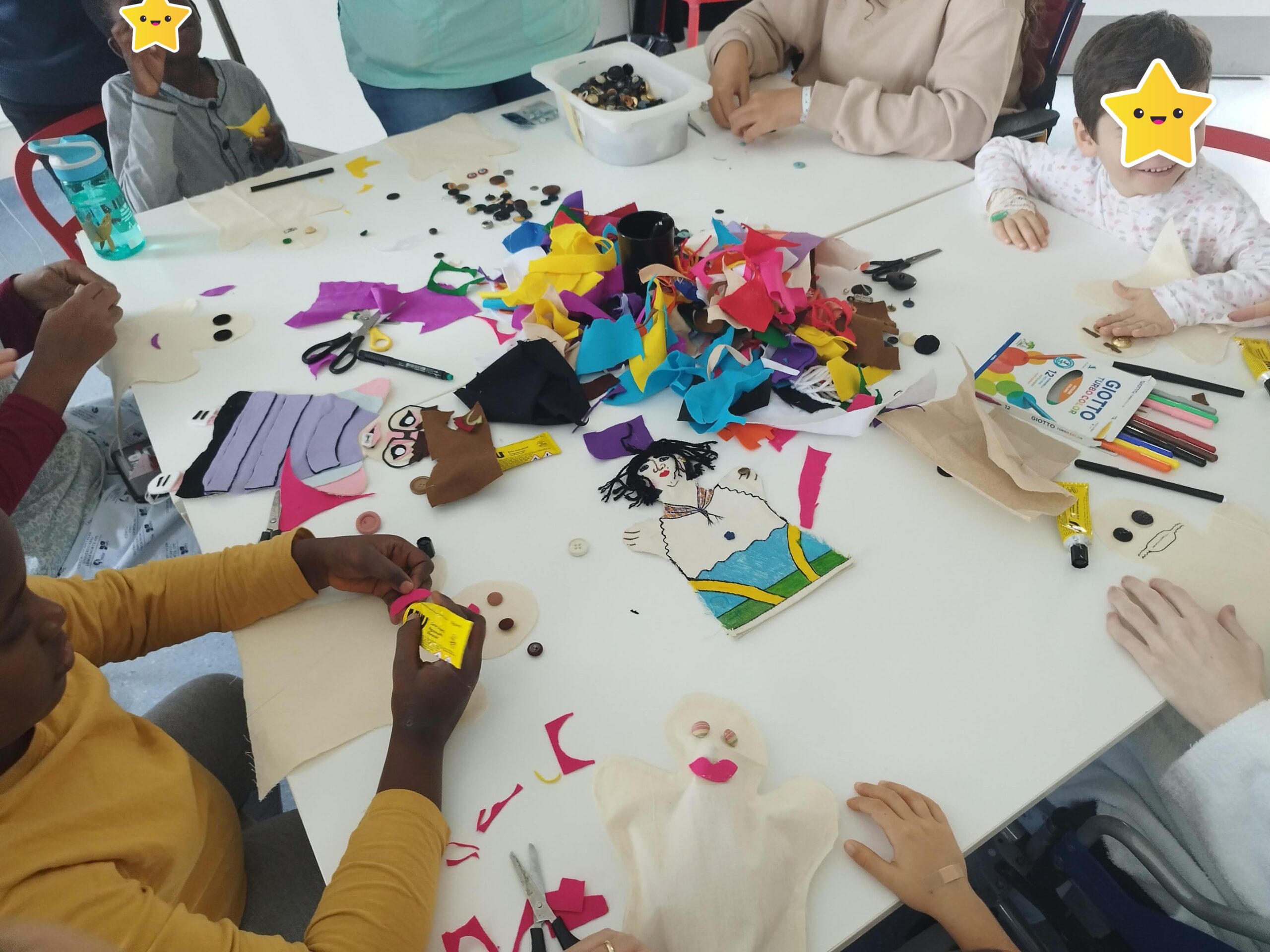 Crianças sentadas à mesa com tecidos coloridos a fazerem marioentas