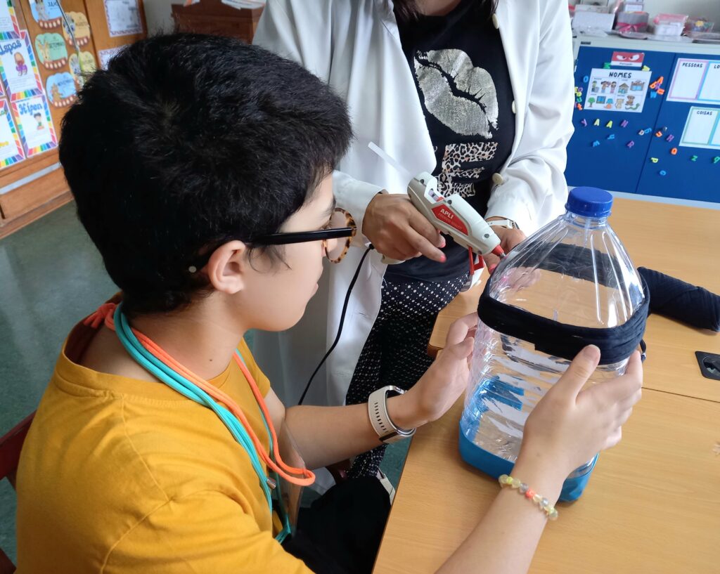 Uma aluna ajuda na construção de um moinho a partir de um garrafão de água.