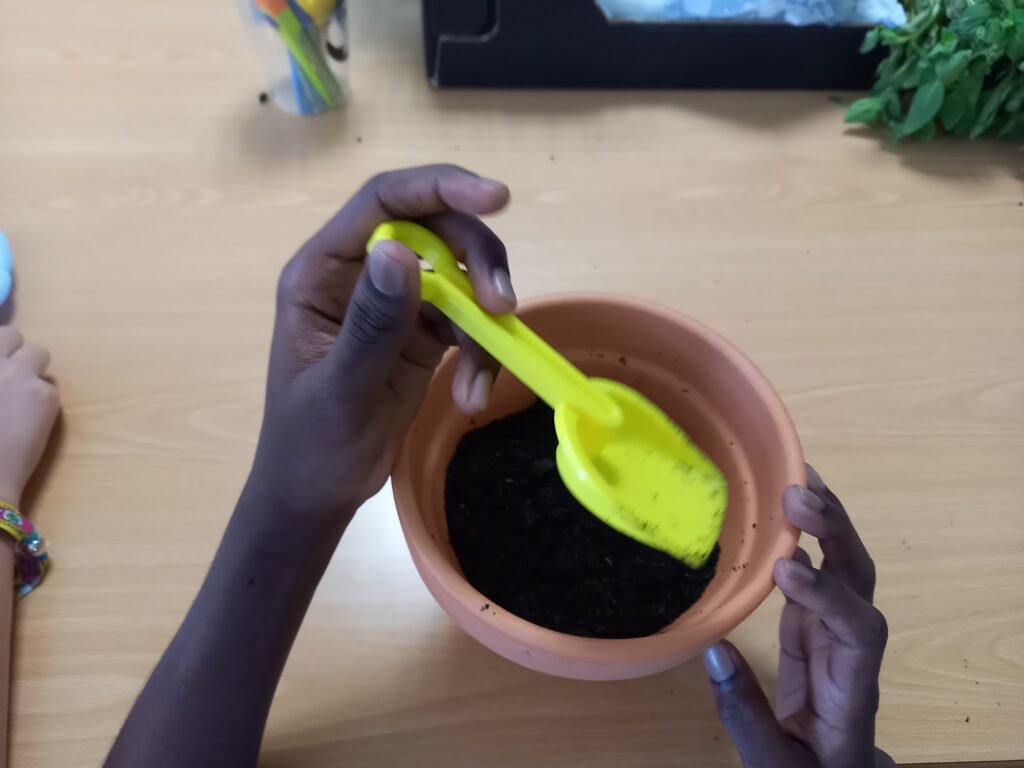 Um aluno a arranjar a terra dentro de um vaso com uma pá para o seu mini-jardim.