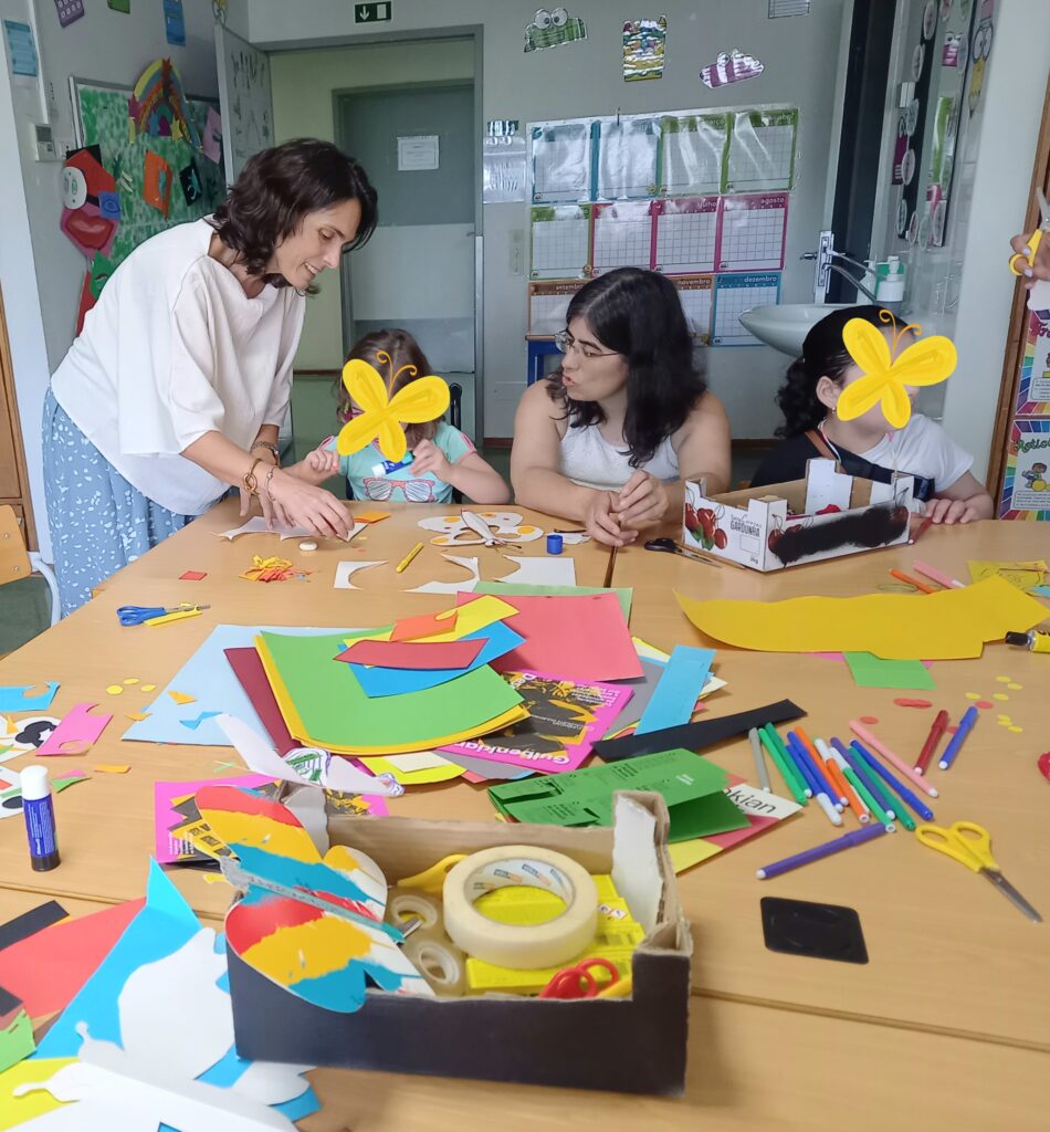 Crianças e adultos à volta de mesas com papeis coloridos