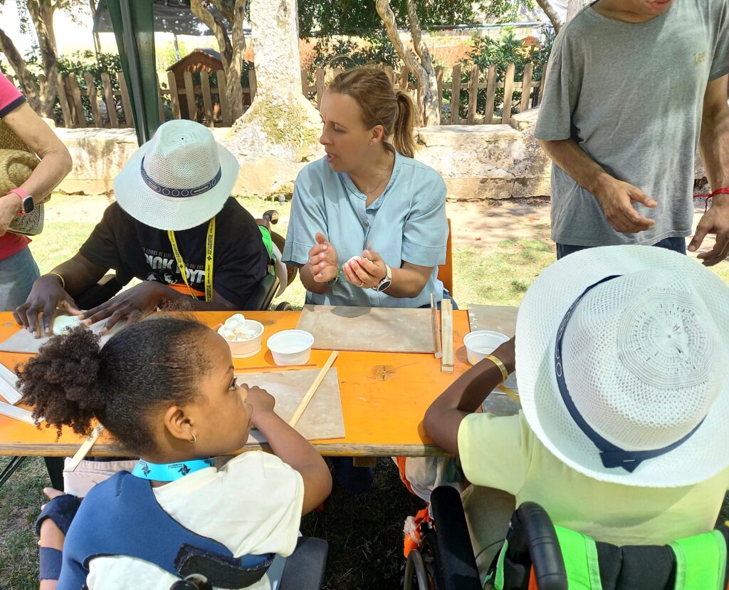 Adultos e crianças junto a zona arborizada realizam actividade de mesa